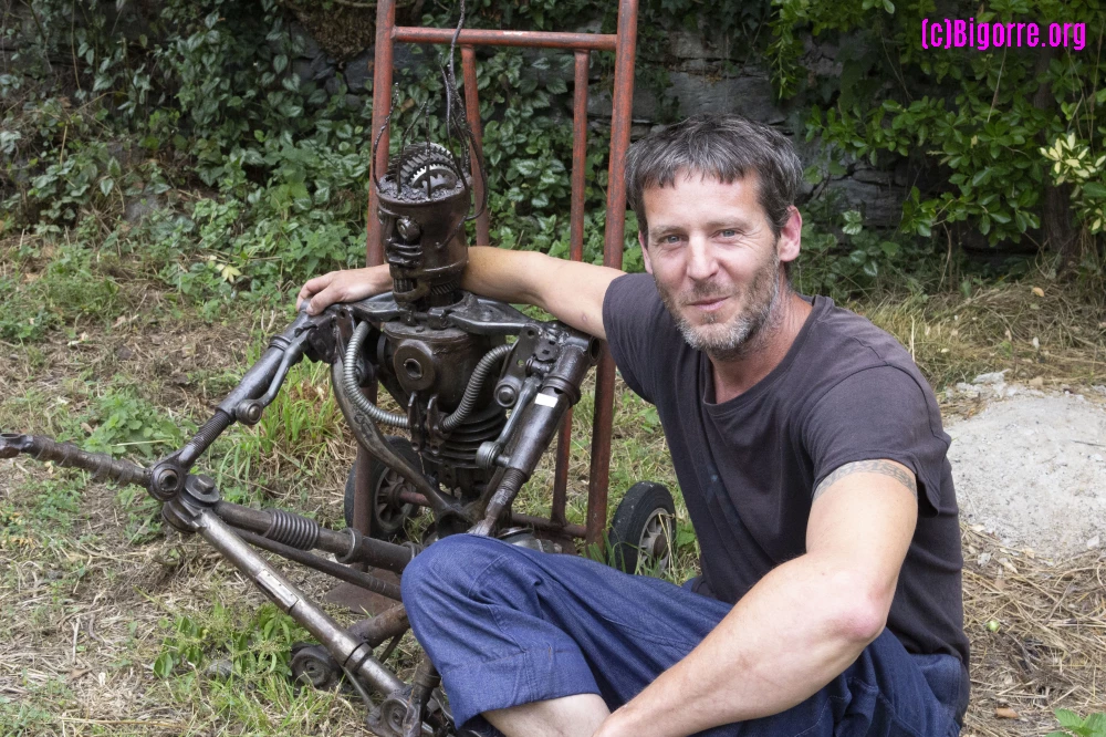 Pedro Fremy assis aux coté de Vétéran dans le jardin de son atelier à Agos-Vidalos
